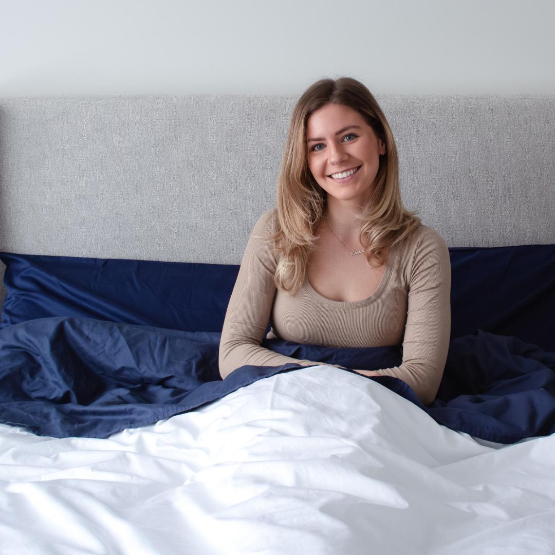 Woman sitting up in bed smiling in Bedface premium sheet set and duvet cover - starlight white and night time navy