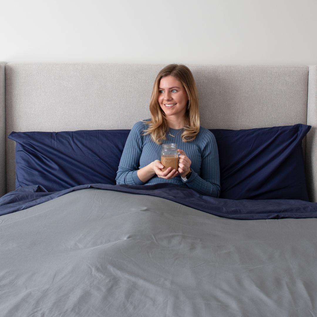 Woman sitting up in bed smiling in Bedface premium sheet set and duvet cover - storm grey and night time navy
